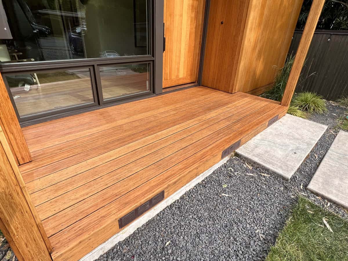 A newly built wooden deck with a sliding glass door, adjacent to a gravel walkway and grass lawn.