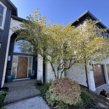 White brick two-story Trusley home in Portland, painted by Pearl Painters; brown garage doors and tree visible. April 2026.