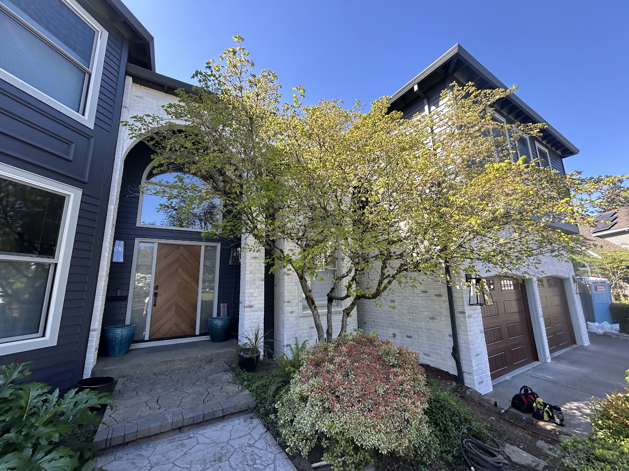 White brick two-story Trusley home in Portland, painted by Pearl Painters; brown garage doors and tree visible. April 2026.