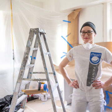 A woman standing next to a painter in a room with paint on it.