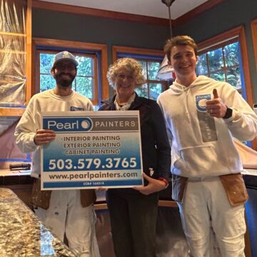 Two painters and a woman in a kitchen hold a Pearl Painters sign with painting services and contact info, Portland.