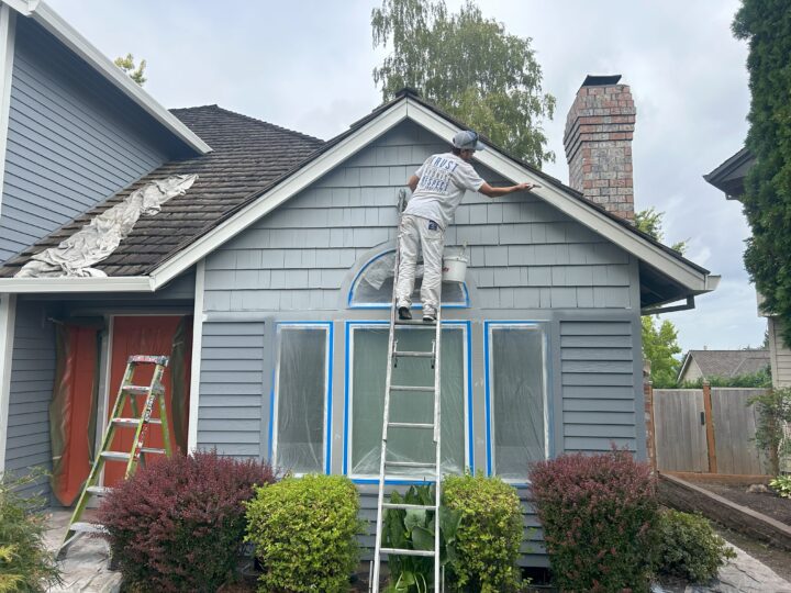 A charming man giving a Beaverton home an exterior paint makeover while on a ladder.