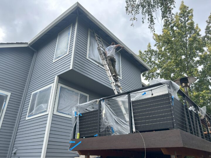 A man on a ladder is giving a charming Beaverton home in the Cooper Mountain Neighborhood an exterior paint makeover.