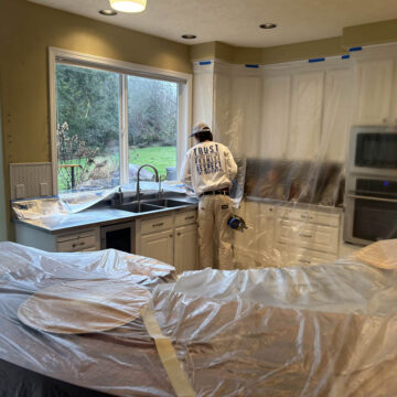 A man is painting a Wilsonville home with high ceilings, using plastic covering.