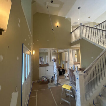 A man is painting a staircase in a Wilsonville home with high ceilings.