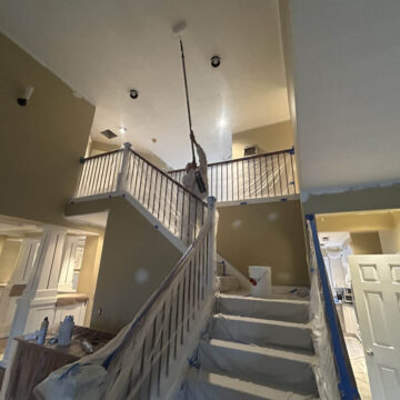 A person painting a staircase in a Wilsonville home with high ceilings.