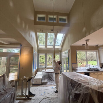 A man is painting the ceiling of a Wilsonville home with high ceilings.