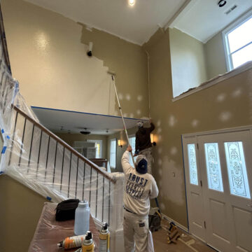 A man painting a staircase in a Wilsonville home with high ceilings.