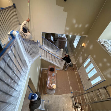 A man is painting a staircase in a Wilsonville home with high ceilings.